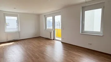 Helles, leeres Wohnzimmer mit Laminatboden und Zugang zu einem Balkon.