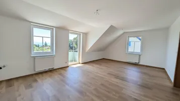Helles, leeres Zimmer mit Laminatboden, Dachschräge und Zugang zu einem französischen Balkon.