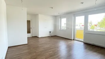 Helles, leeres Wohnzimmer mit Laminatboden und Zugang zu einem kleinen Balkon.