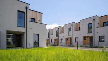 Reihenhäuser mit moderner Architektur, weißen Fassaden, Holzakzenten und grüner Rasenfläche.