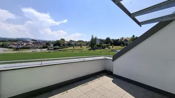 Geräumige Terrasse mit Fliesenboden, Glasüberdachung und weitem Blick über grüne Landschaft.