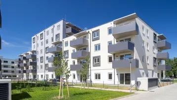 Modernes Mehrfamilienhaus mit weißer und grauer Fassade, Balkonen und gepflegten Grünflächen unter blauem Himmel.