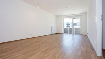 Helles, leeres Wohnzimmer mit Laminatboden und Zugang zu einem Balkon in einem Neubau.
