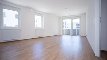 Helles, leeres Zimmer mit Laminatboden, weißen Wänden und Zugang zu einem Balkon.