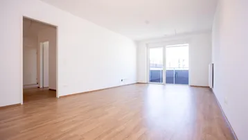 Helles, leeres Zimmer mit Laminatboden und Zugang zu einem Balkon, ideal als Wohnbereich.
