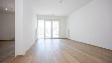 Helles, leeres Zimmer mit Holzboden und Zugang zu einem Balkon, ideal für einen Wohnbereich.