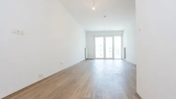 Helles, unmöbliertes Wohnzimmer mit Laminatboden und Zugang zu einem großen Balkon.