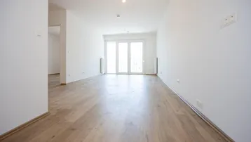 Helles, leeres Wohnzimmer mit modernem Laminatboden und Zugang zu einem Balkon oder einer Terrasse.