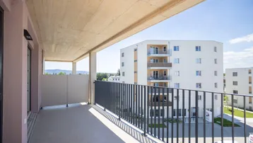 Geräumiger Balkon mit moderner Brüstung und Blick auf die umliegenden Neubauten und Berge.