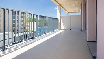 Langer, sonniger Balkon mit Betonboden und Metallgeländer, bietet einen Blick auf die Umgebung.