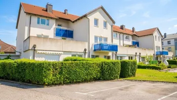 Modernes Mehrfamilienhaus mit blauen Balkonen, umgeben von gepflegten Hecken und Grünflächen.
