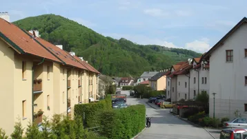 Wohnsiedlung mit Reihenhäusern und Blick auf die umliegende grüne Hügellandschaft und Berge.
