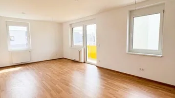 Helles, leeres Wohnzimmer mit Parkettboden, großen Fenstern und Zugang zum Balkon.