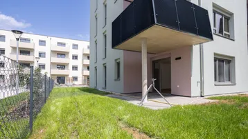 Neubau-Fassade mit Balkon und angrenzender Rasenfläche bei sonnigem Wetter.