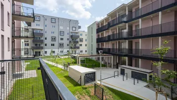 Moderne Wohnanlage mit mehreren Gebäuden, Balkonen und begrüntem Innenhof unter blauem Himmel.