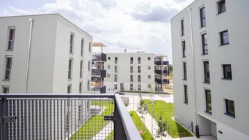 Blick von einem Balkon auf moderne Wohngebäude mit Grünflächen und weiteren Balkonen.