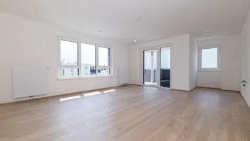 Helles und geräumiges Wohnzimmer mit großen Fenstern, Holzboden und Zugang zum Balkon.