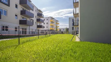 Moderne Wohngebäude mit Balkonen und einer weitläufigen Grünfläche im Vordergrund.