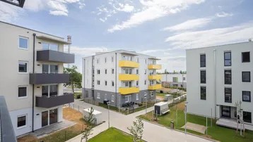 Moderne Wohngebäude mit farbigen Balkonen und gepflegten Grünflächen in einer neuen Wohnsiedlung.