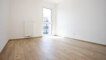 Helles Zimmer mit weißen Wänden, modernem Laminatboden und großem Fenster.