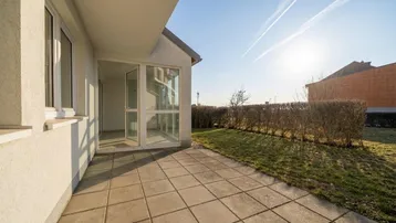 Sonniger Außenbereich mit gepflasterter Terrasse und angrenzender Rasenfläche.