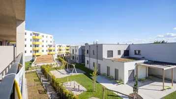 Weitläufiger Gemeinschaftsgarten mit Spielplatz und modernen Wohngebäuden unter blauem Himmel.