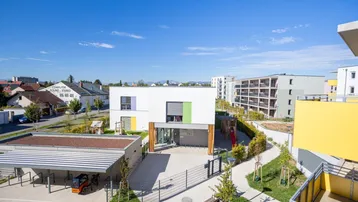 Weitläufige Außenansicht einer modernen Wohnanlage mit Spielplatz und Grünflächen unter blauem Himmel.