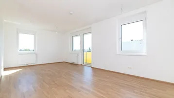 Helles, leeres Zimmer mit Laminatboden, weißen Wänden und Zugang zu einem Balkon.