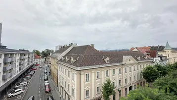 Weitläufiger Blick über die Stadt mit historischen Gebäuden, Straßen und bewölktem Himmel.