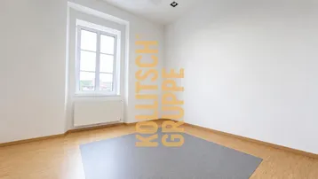 Heller, leerer Raum mit weiß gestrichenen Wänden, Holzfußboden und einem Fenster für natürliches Licht.