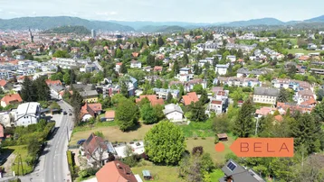 Luftaufnahme einer grünen Wohngegend mit Häusern, Bäumen und Bergen im Hintergrund, die eine weite Aussicht bietet.