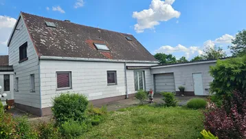 Einfamilienhaus mit Satteldach, weißer Fassade und großem Gartenbereich unter blauem Himmel.