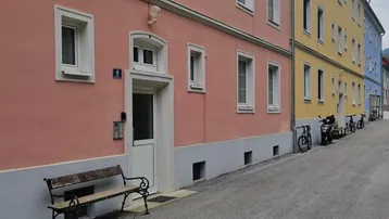 Ansicht einer Wohnstraße mit mehrstöckigen Gebäuden in Pastellfarben und einer Sitzbank.