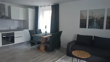 Heller offener Wohnbereich mit integrierter Küche, Esstisch und Sofa in modernem Stil.