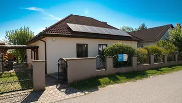 Einfamilienhaus mit gepflegtem Vorgarten, Zaun und Photovoltaikanlage auf dem Dach.