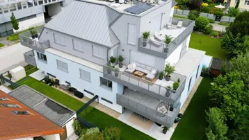 Moderne Wohnanlage mit mehreren möblierten Terrassen, Grünflächen und Solaranlage auf dem Dach.