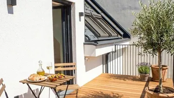 Sonnige Terrasse mit Holzboden und kleinem Tisch, ideal für entspannte Mahlzeiten im Freien.