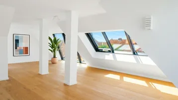 Helles und geräumiges Dachgeschosszimmer mit Holzboden, großen Dachfenstern und Blick auf die Stadt.