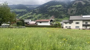 Weitläufige Wiese mit Blick auf umliegende Häuser und die majestätische Berglandschaft unter bewölktem Himmel.