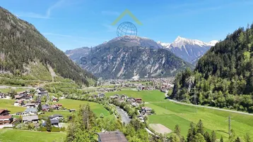 Atemberaubender Weitblick über ein grünes Tal mit einem Dorf und majestätischen Bergen im Hintergrund.