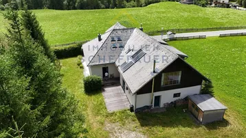 Luftaufnahme eines Hauses mit Holzterrasse, umgeben von grünen Wiesen und Bäumen.