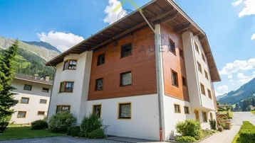 Modernes Mehrfamilienhaus mit Holzverkleidung und Bergblick unter blauem Himmel.