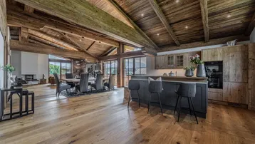 Geräumiger offener Wohn- und Essbereich mit Holzbalkendecke, Eichenparkett und integrierter Küche im Chalet-Stil.