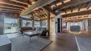 Geräumiges Wohnzimmer mit Holzbalkendecke, großen Fenstern und gemütlicher Sitzecke.