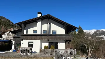 Großzügiges Haus mit Holzterrasse und Bergblick, umgeben von winterlicher Landschaft.