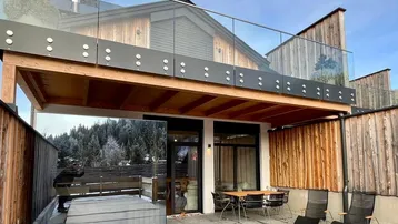 Moderne Terrasse mit Whirlpool, Essbereich und Balkon, umgeben von einer verschneiten Berglandschaft.