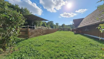 Großer, sonniger Gartenbereich mit Rasenfläche und Holzzaun, umgeben von Bäumen und Natur.