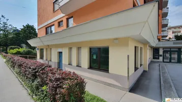 Gebäudeansicht von außen mit einer niedrigen Hecke entlang des Bürgersteigs und einer hellen Fassade.
