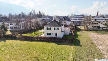 Luftaufnahme eines Einfamilienhauses mit großem Grundstück und Bergblick in sonniger Lage.