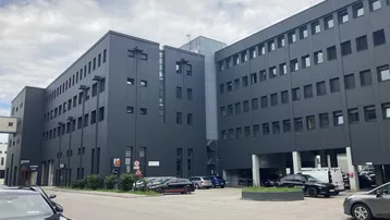 Modernes Geschäftsgebäude mit dunkler Fassade und Parkplätzen davor unter bewölktem Himmel.